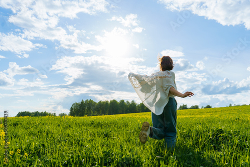 Tablou pe pânză a young girl in a boho cape runs through a green field with yellow flowers