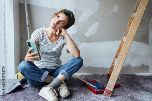 Young woman with cell phone thinking how to renovate her apartment