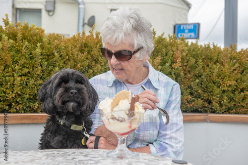 Active senior woman sitting with black cockapoo dog eating ice cream 