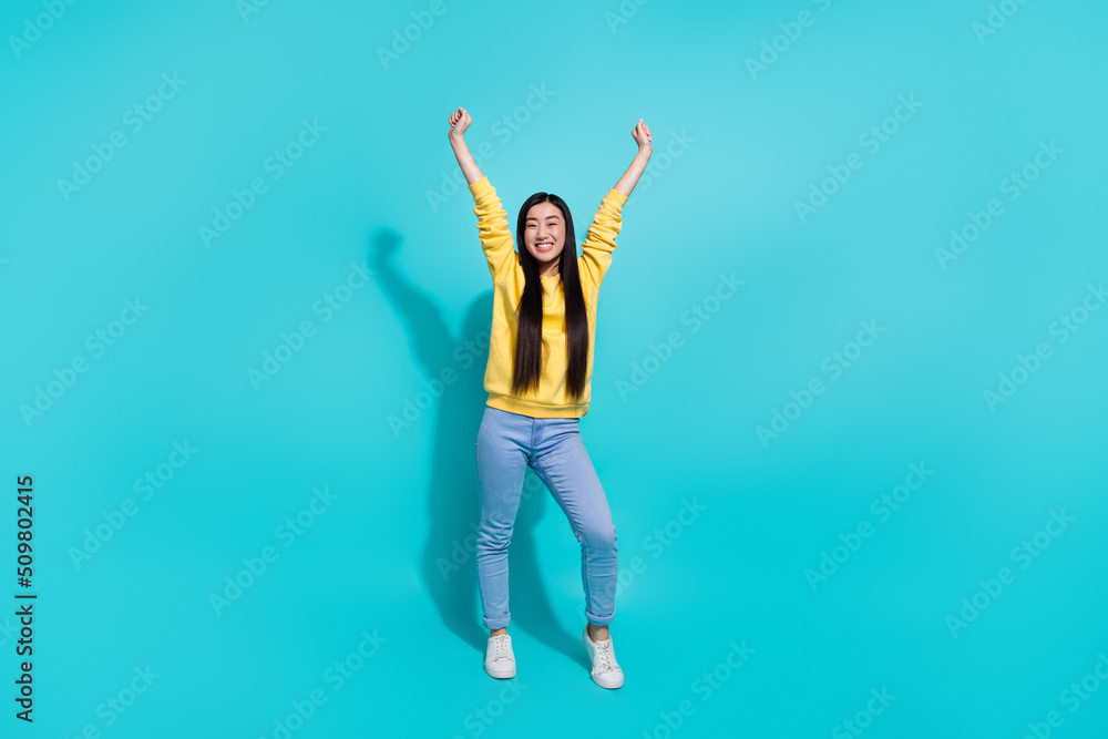 Full length photo of impressed lucky woman wear yellow pullover rising fists isolated teal color background Full length photo of impressed lucky woman wear yellow pullover rising fists isolated teal color background
