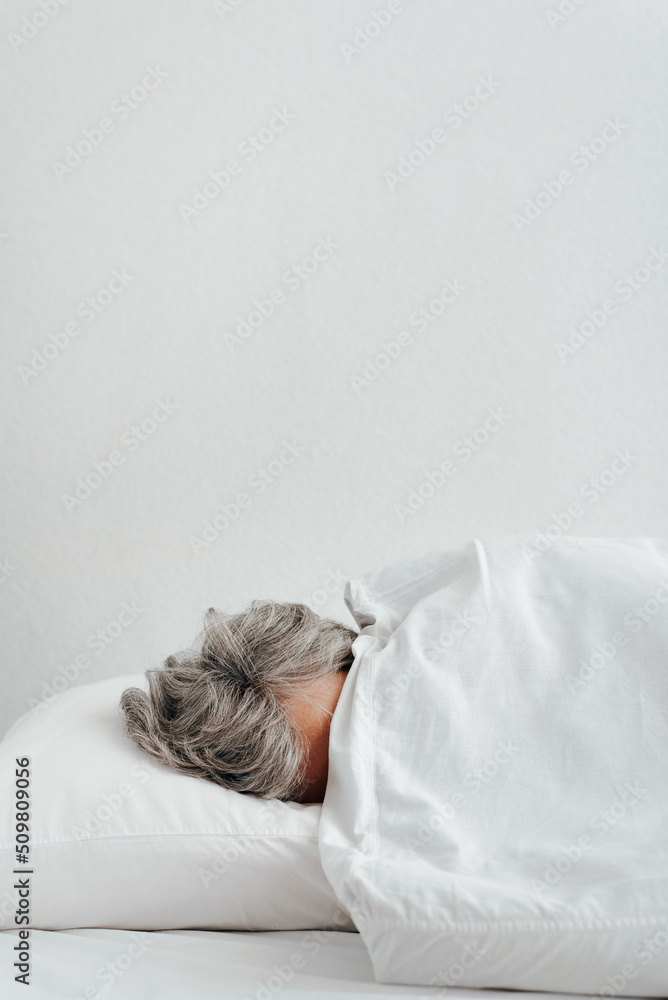 Concept depression, frustration, laziness, stress. Side view of tired woman with gray hair covered with blanket lying on bed in bedroom. Vertical view, copy space Concept depression, frustration, laziness, stress. Side view of tired woman with gray hair covered with blanket lying on bed in bedroom. Vertical view, copy space