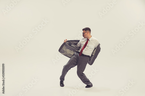 Portrait of young man, businessman dressed in suit in 50s, 60s fashion style dancing isolated on white background. Retro vintage style, business, ad, emotions