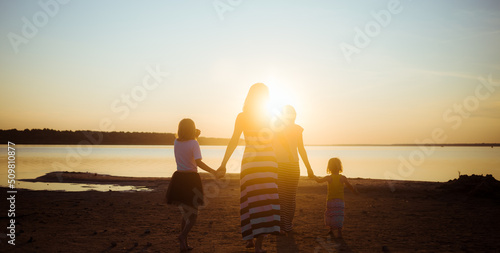 Φωτογραφία Silhouettes of children and mother walking hand in hand on the sea beach to sunset light