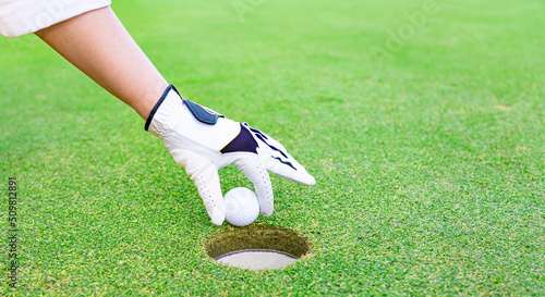 A gloved hand takes a golf ball out of the hole