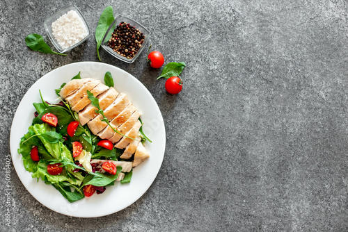 Grilled chicken breast and salad with tomato, spinach, asberg, radichio, arugula on a stone background with copy space for your text photo