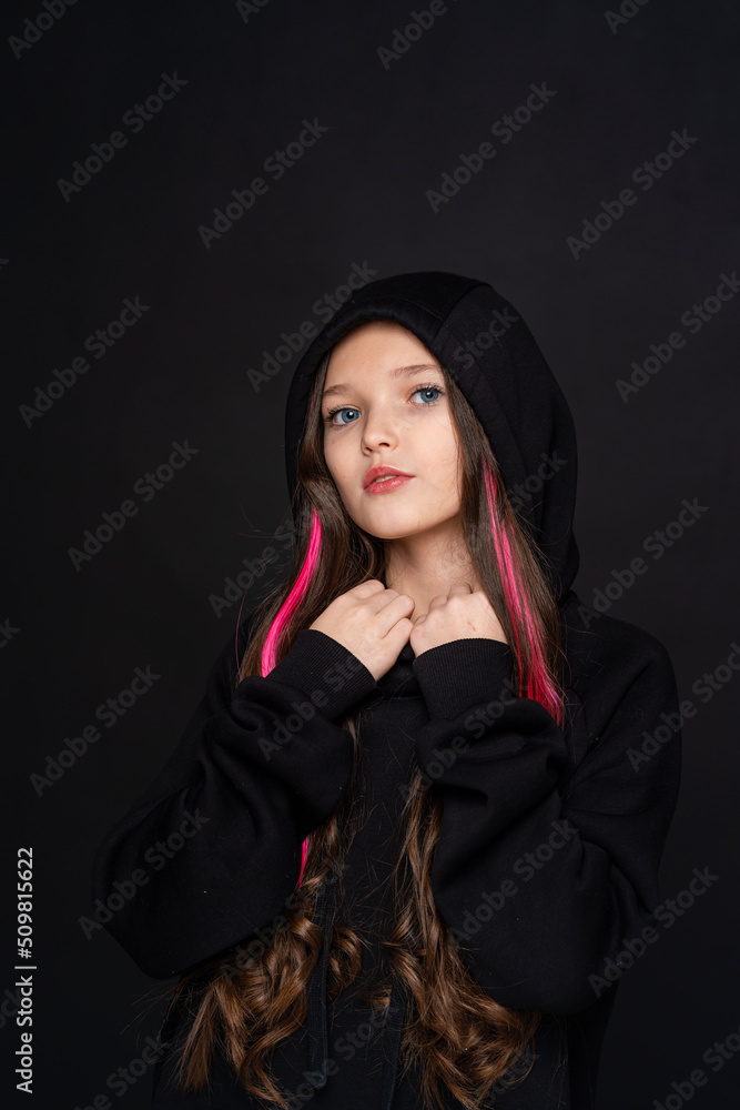 stylish teenage girl with dark hair with pink strands, dressed in fashionable clothes, hoodie with hood, stands on black background and looks at camera. transitional age. concept of youth and clothing stylish teenage girl with dark hair with pink strands, dressed in fashionable clothes, hoodie with hood, stands on black background and looks at camera. transitional age. concept of youth and clothing