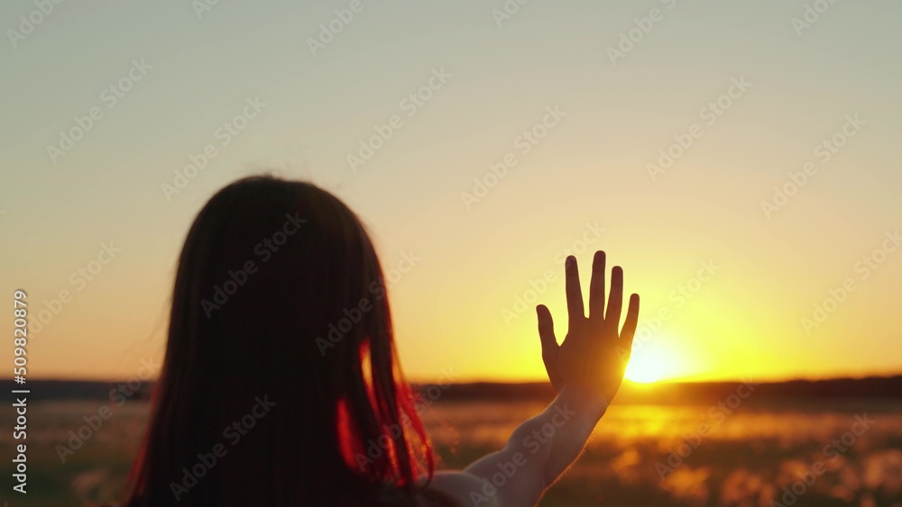 Happy girls stretches her hand to sun. Glare of sunset on fingers of young woman. Prayer of woman, religion of world. Girl travels at sunset. Silhouette of hand in sun. Girl walk at sunset. Prayer god
