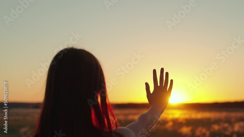 Happy girls stretches her hand to sun. Glare of sunset on fingers of young woman. Prayer of woman, religion of world. Girl travels at sunset. Silhouette of hand in sun. Girl walk at sunset. Prayer god