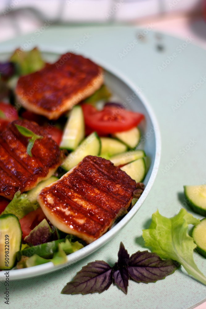 Grilled halloumi cheese served on vegetable salad with tomato, cucumber and lettuce on the plate Grilled halloumi cheese served on vegetable salad with tomato, cucumber and lettuce on the plate