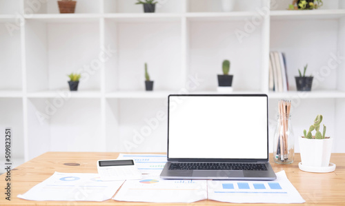 Close up of modern office desktop with blank white notebook screen, smartphone, coffee cup, supplies and other items. Mock up