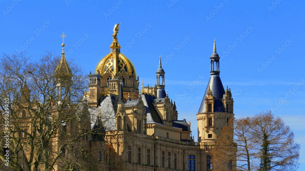 malerische Dachkonstruktion des Schweriner Schlosses mit Türmen und vergoldeter Kuppel zwischen Bäumen