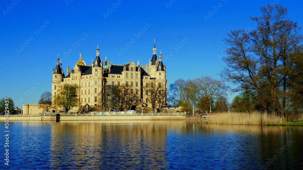 prächtiges Schloss in Schwerin am Burgsee am  Abend neben Schilf und Bäumen unter blauem Himmel