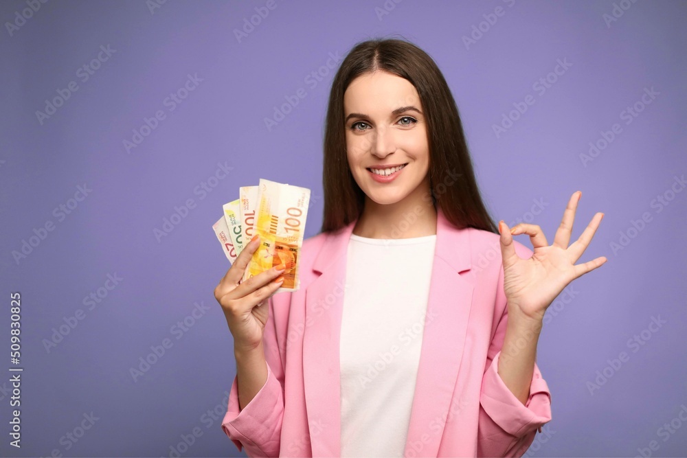 Beautiful woman holding israel shekels doing ok sign with fingers, smiling friendly gesturing excellent symbol Beautiful woman holding israel shekels doing ok sign with fingers, smiling friendly gesturing excellent symbol