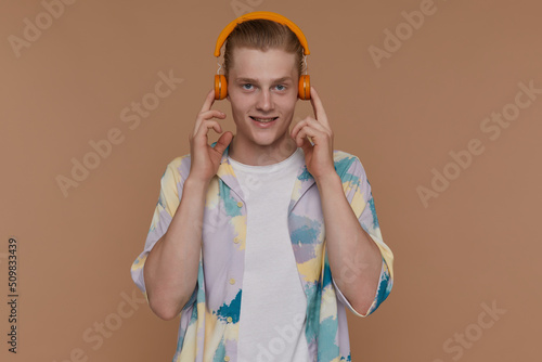 Indoor portrait of young blonde man posing over beige background looking into camera while listening music