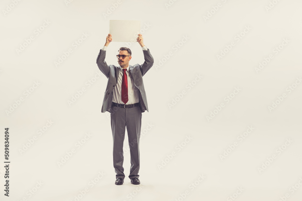 One man, businessman wearing grey striped suit in 50s, 60s fashion style standing blank sheet of paper isolated on white background. Retro vintage style, business, ad One man, businessman wearing grey striped suit in 50s, 60s fashion style standing blank sheet of paper isolated on white background. Retro vintage style, business, ad