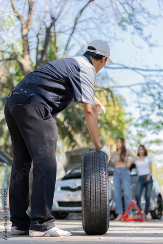 Expertise mechanic man in uniform holding a tire for help a woman for changing car wheel on the highway, car service, repair, maintenance concept.