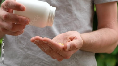 Close up shot of a man pouring yellow pills from white plastic bottle into hand. Slow motion.