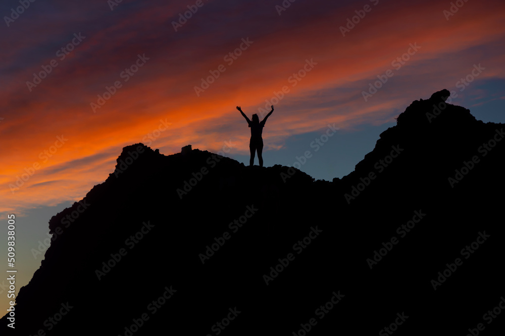Silhouette of the girl on top of the rocks. Beautiful colorful sunset sky. Punta de Teno, near Buenavista del Norte, Santa Cruz de Tenerife.