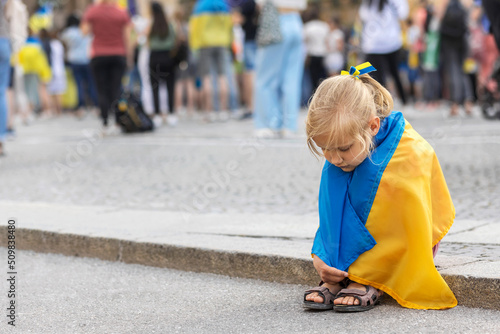Ukraine Child with the flag of Ukraine is crying. Children refugees on Support Rally in Europe. Sadness longing hope. Anti war Protest in Europe. © Maryana