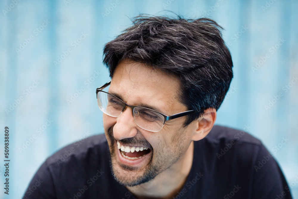A brunette man with a beard in glasses laughs on a blue background. white teeth and sincere emotions A brunette man with a beard in glasses laughs on a blue background. white teeth and sincere emotions
