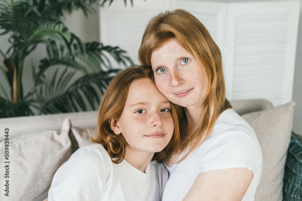 Mom and daughter with red hair. Mom and daughter teen hugging at home on the couch. 