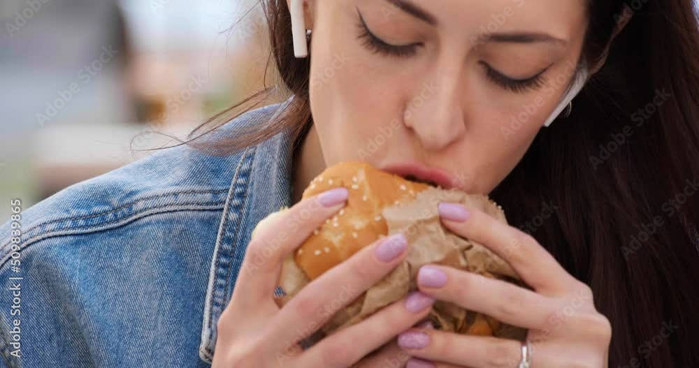 Beautiful young woman eating tasty burger outdoors, closeup Beautiful young woman eating tasty burger outdoors, closeup