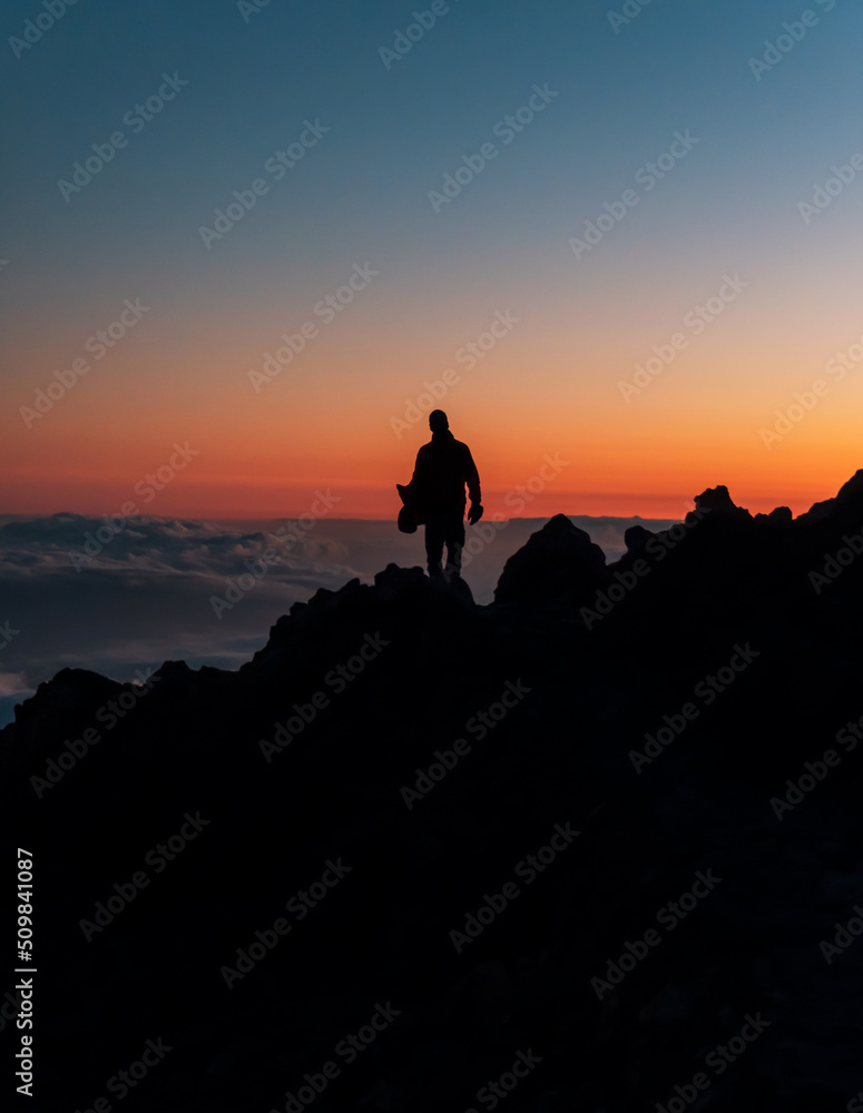 Silhouette of the person on top of the rocks during sunset on the peak of Mount Teide called 'Pico del Teide'. Teide National Park, Tenerife, Canary islands, Spain.