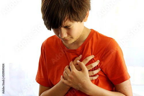 Teenager boy Caucasian holding his chest suffering from pain. Abnormal coronary artery course or origin, or diseases of heart muscle heart attack in children concept. photo