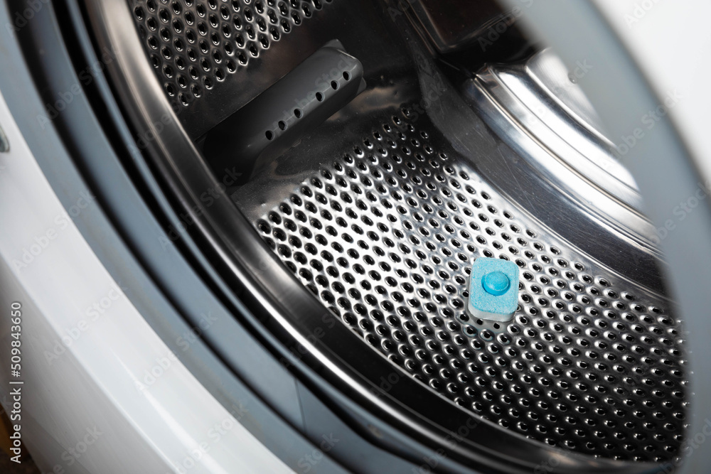Capsule with liquid powder in the washing machine with laundry, close-up. Gel for washing in the car. Colorful eco-gel for washing in capsules. Washing clothes. Purity concept