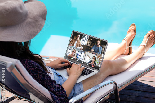 Young caucasian woman video conferencing with coworkers through laptop on poolside during vacation