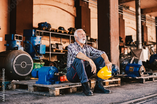A tired senior factory worker sitting on the pallet at the facility and taking a break after hard work. © dusanpetkovic1