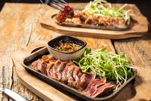 sirloin steak on a hot pan on a wooden plate with dipping sauce decorated with sunflower sprouts,World food day