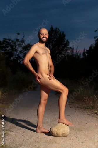 Young male fully naked standing on a trail at night