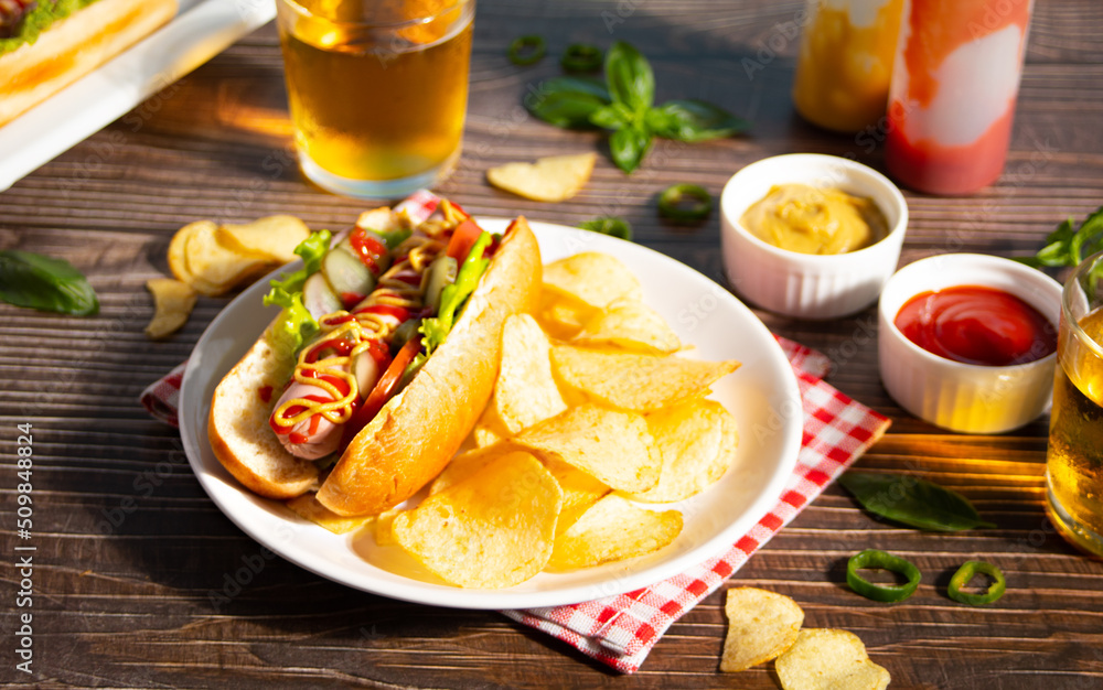 Delicious homemade hotdogs with chips and glasses of beer on wooden table. Delicious homemade hotdogs with chips and glasses of beer on wooden table.