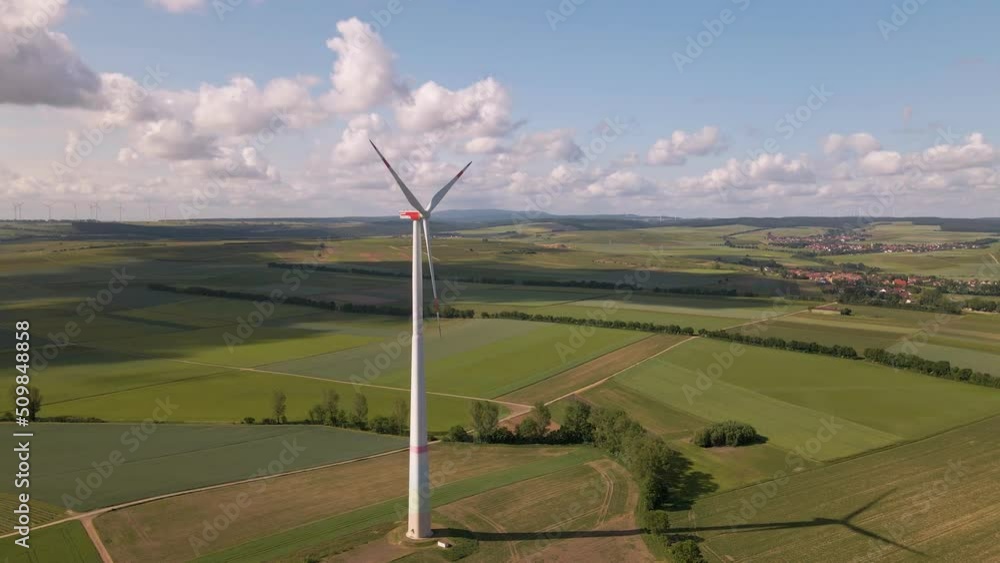 Tall white wind mill standing in an expansive field underneath soft cumulus clouds on a sunny day in Europe. Aerial rotating approach Tall white wind mill standing in an expansive field underneath soft cumulus clouds on a sunny day in Europe. Aerial rotating approach