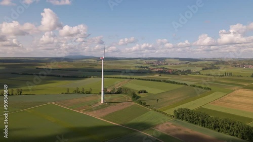 Drone footage of approaching flight towards a tall wind mill underneath soft cumulus clouds in rural Germany. photo