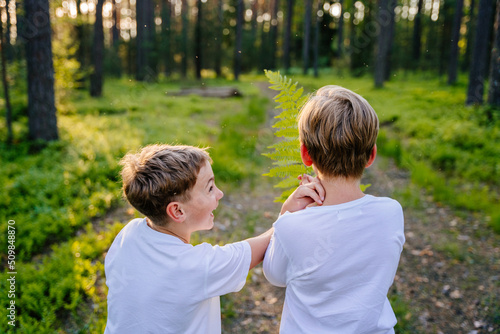 Summer vacation for inquisitive kids in forest. Rear view of of two happy friends boys looking through fern having fun together in nature. © Iryna