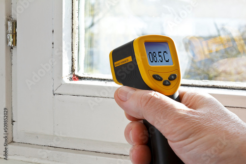 Male hand with an infrared or laser thermometer, measuring the temperature of a window seal where mildew is growing. photo
