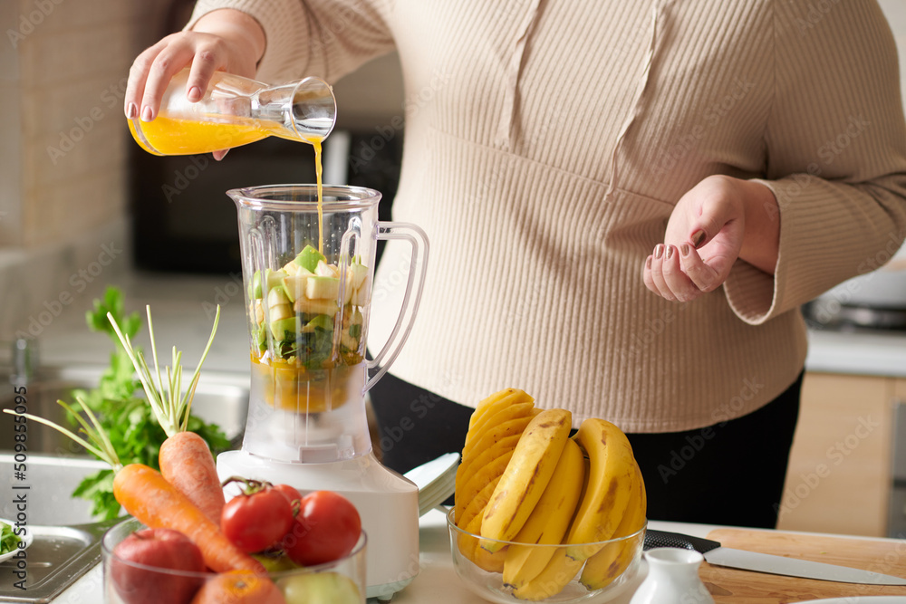 Cropped image of plus size woman adding orange juice in blender with