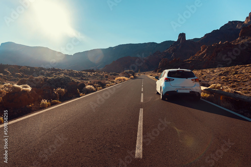White car on the road in the Teide national park in the early morning. Surrounded by mountains and volcanic landscape. Tenerife, Canary islands, Spain.