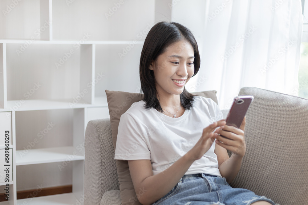 Asian woman sitting with smart phone on sofa in living room, Looking at tablet screen, Relaxing at home, Working through the Internet communication system, Happy working lifestyle. Asian woman sitting with smart phone on sofa in living room, Looking at tablet screen, Relaxing at home, Working through the Internet communication system, Happy working lifestyle.
