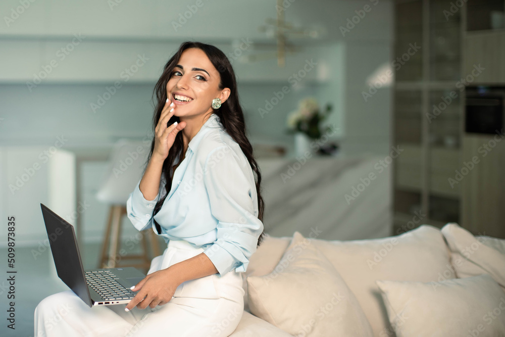 Woman sitting on sofa indoors at home apartment, using laptop computer, self employed remote work and small business freelancer, education and leisure time, online shopping, leisure time and relax Woman sitting on sofa indoors at home apartment, using laptop computer, self employed remote work and small business freelancer, education and leisure time, online shopping, leisure time and relax