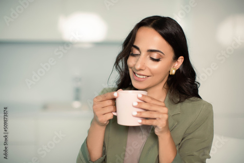Smiling woman holding mug of coffee or tea, indoors at home in apartment, enjoying leisure time, morning or start of the day, relaxation and cozy, confident and independent