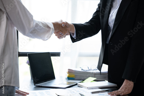 Closeup of handshaking above working table with laptop and paperworks for successful dealing agreement.