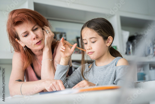 Friendly mother helping to her daughter to do homework