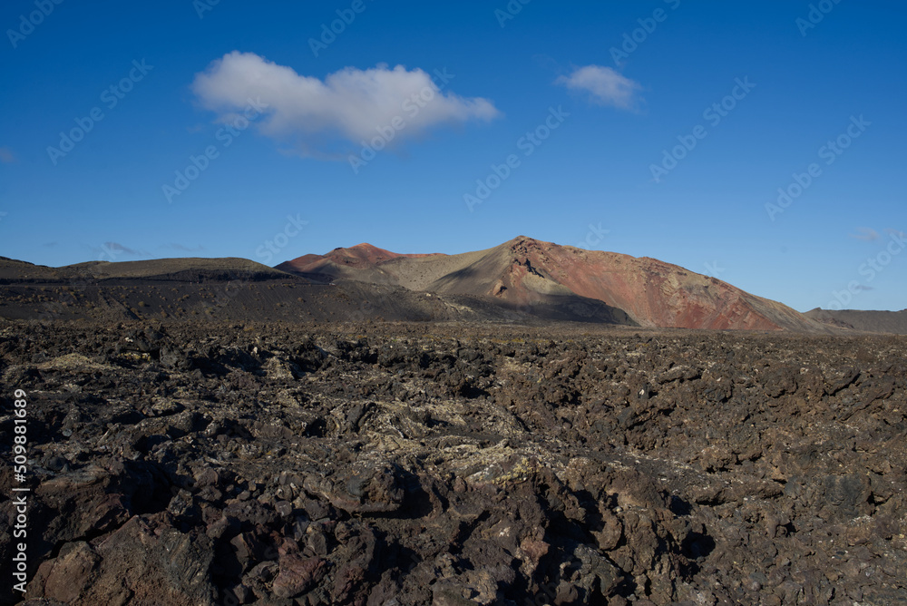 Volcanic lava sediments with a volcano in the background in Timanfaya National park, Lanzarote island, Spain.