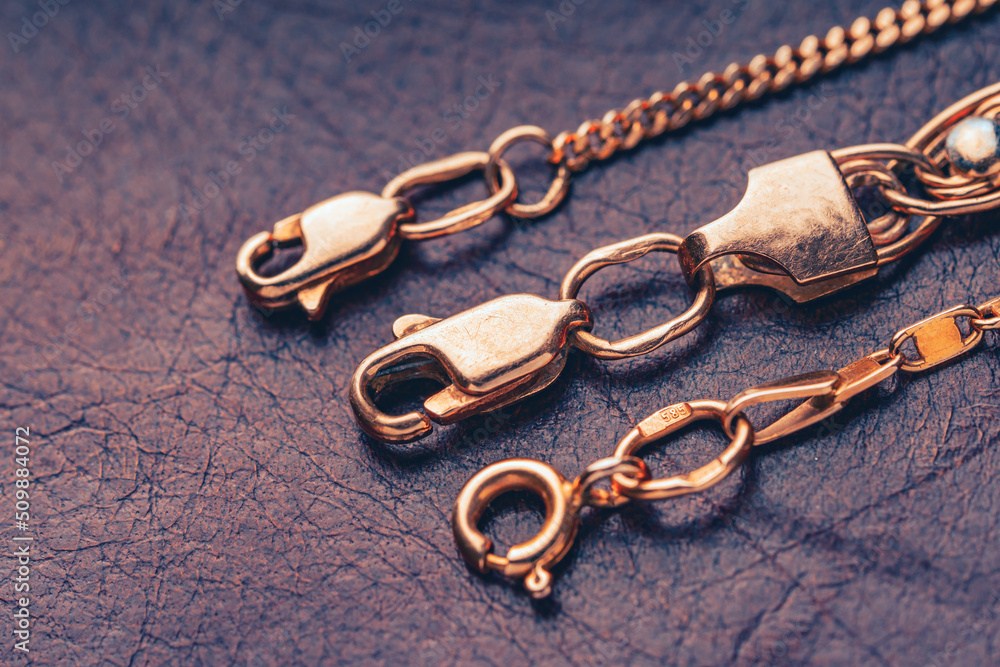 Gold clasps of a golden chains lying on a leather background. Macro photography with soft focus. - obrazy, fototapety, plakaty 