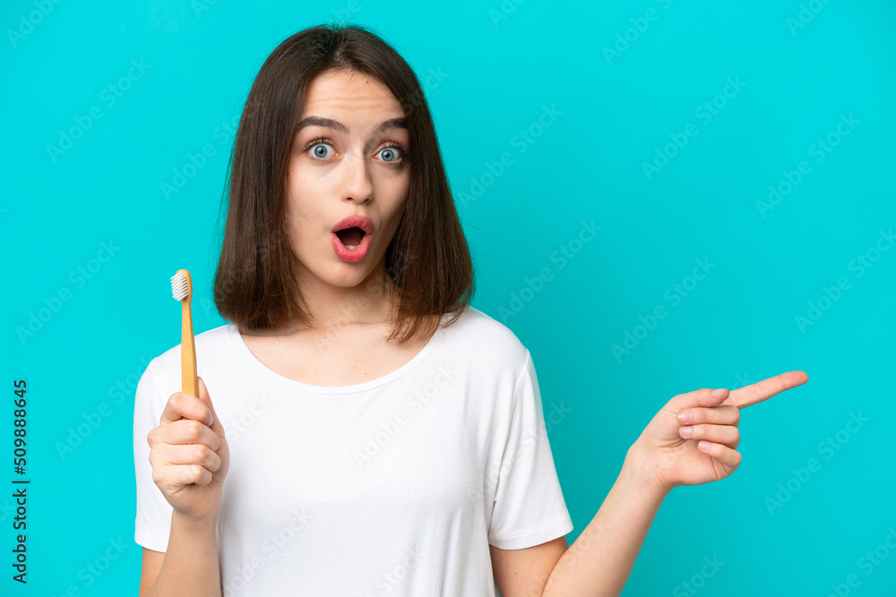 Young Ukrainian woman brushing teeth isolated on blue background surprised and pointing side Young Ukrainian woman brushing teeth isolated on blue background surprised and pointing side