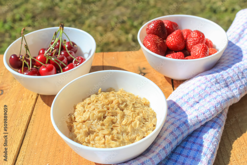 Oatmeal on a wooden table in a white plate. Various berries in the background. Healthy food concept. Breakfast is rich in vitamins. Village atmosphere. Oatmeal on a wooden table in a white plate. Various berries in the background. Healthy food concept. Breakfast is rich in vitamins. Village atmosphere.