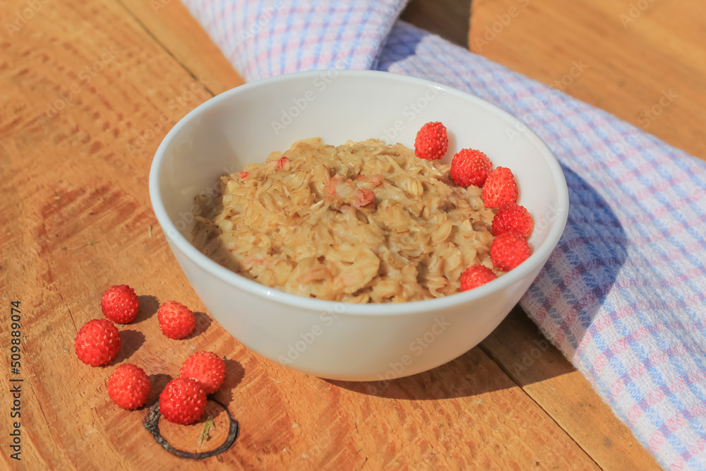 Oatmeal with wild strawberries in a plate on a wooden table. Red small berries are rich in vitamins. Healthy food for breakfast Oatmeal with wild strawberries in a plate on a wooden table. Red small berries are rich in vitamins. Healthy food for breakfast